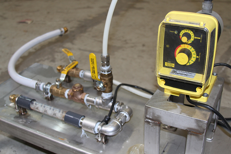 Une pompe doseuse reliée à des tuyaux et des flexibles sur un patin de dosage de polymères liquides.