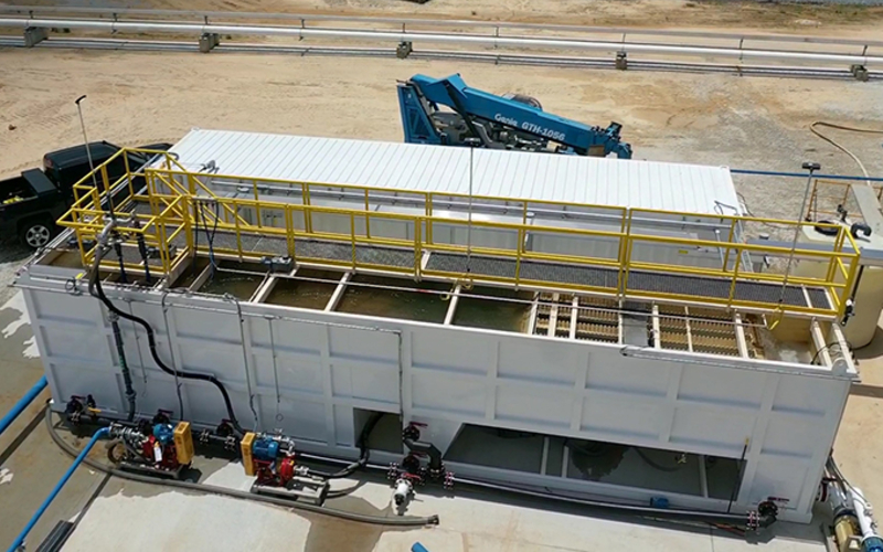 A picture looking down at an angle at a large white stationary water clarifier with a truck and other industrial equipment at a job site.