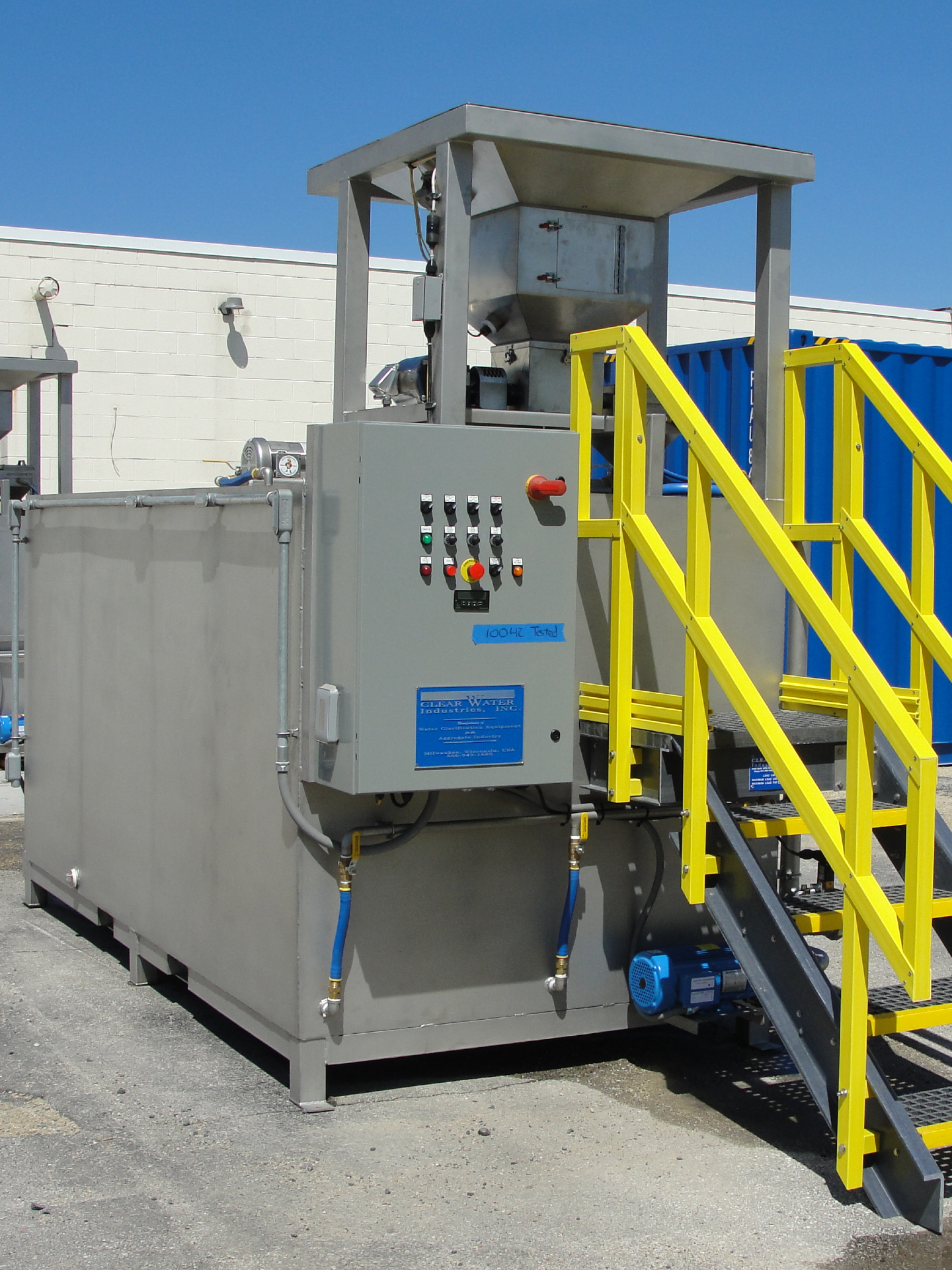 A large stainless steel dry polymer preparation system built to hold 1650 lbs. big bags pictured outside of a building.