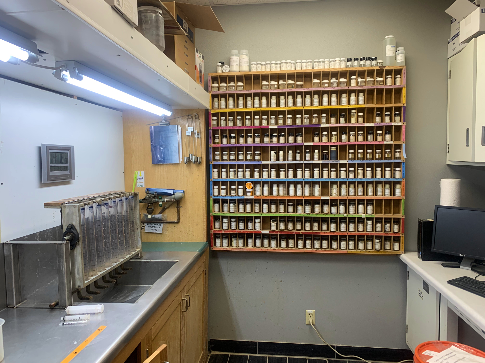 Lab A small room with beakers over the sink of the left and a wall of different chemicals in the back.