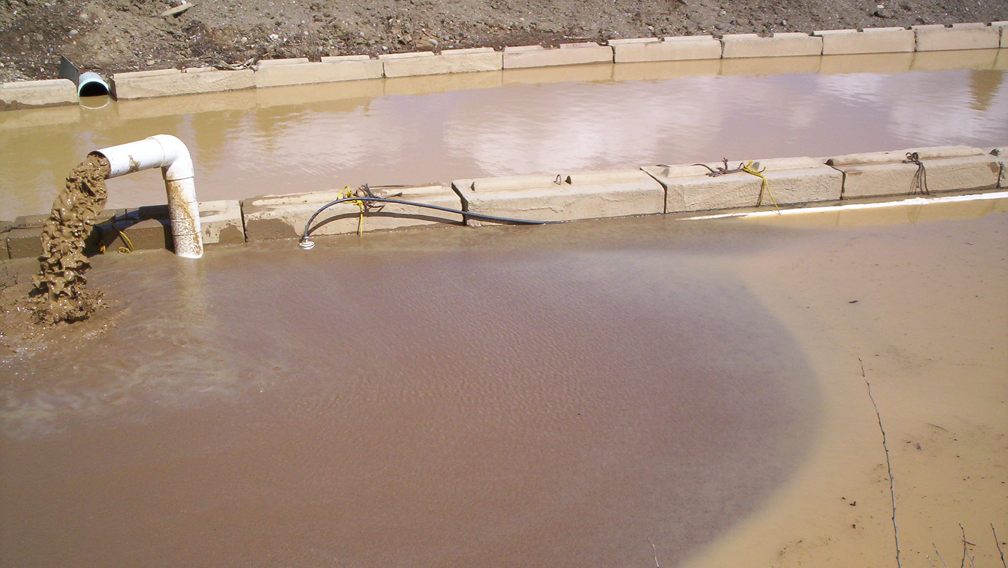 Dirty water pumping out of a pipe into a dirty water cell with another dirty water cell filled behind it.