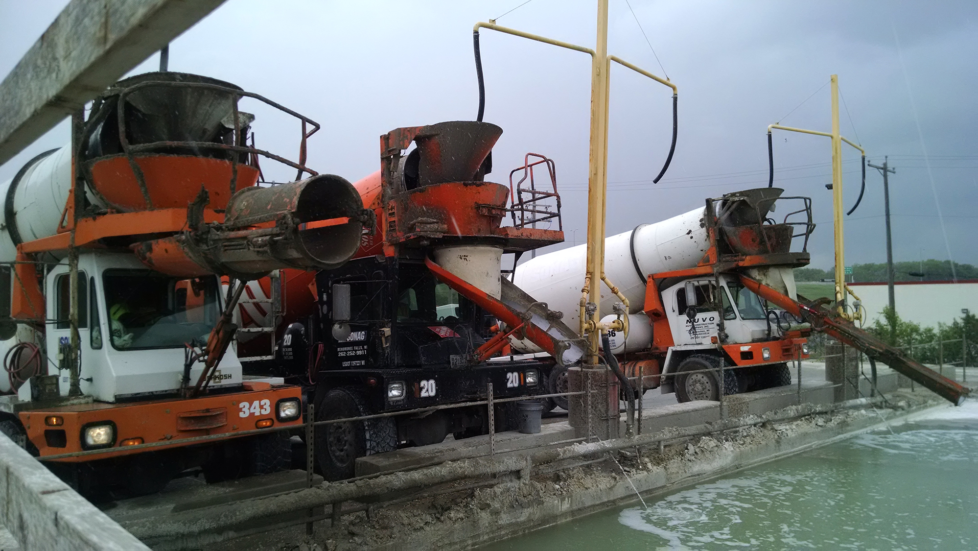 Three cement trucks with white and red paint lined up at a concrete washout pond.