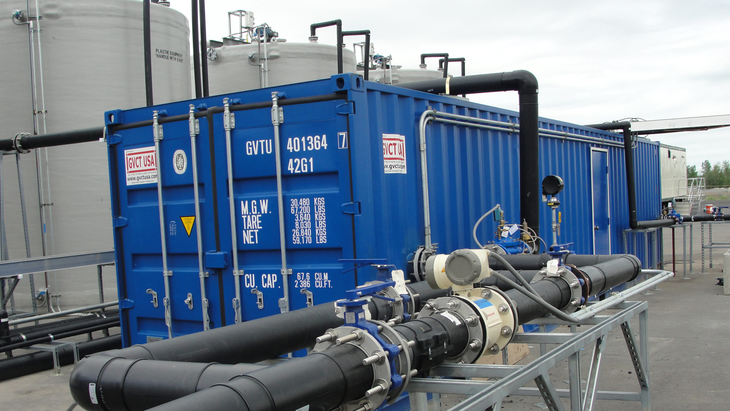 Piping running over a shipping container and connecting to tanks behind the shipping container.