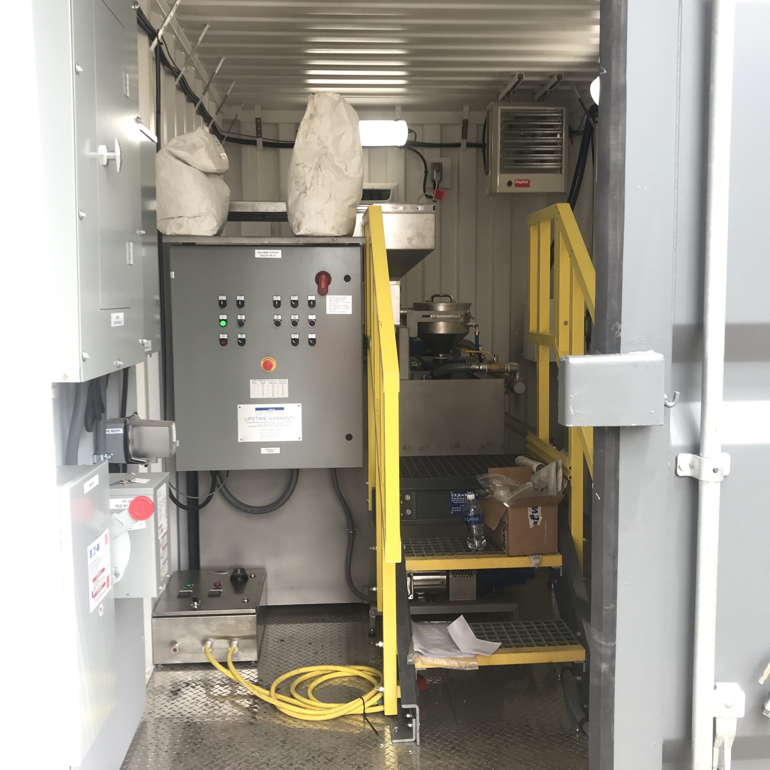 A dry polymer preparation machine in a climate-controlled shipping container with polymer bags on top of the control panel.