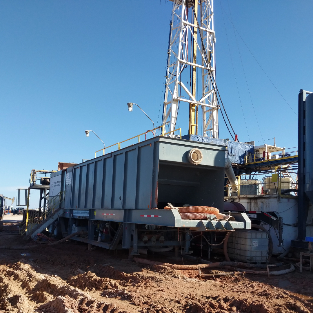 A rectangular portable industrial water clarifier pictured at an angle with a drilling and tunneling rig in the background.