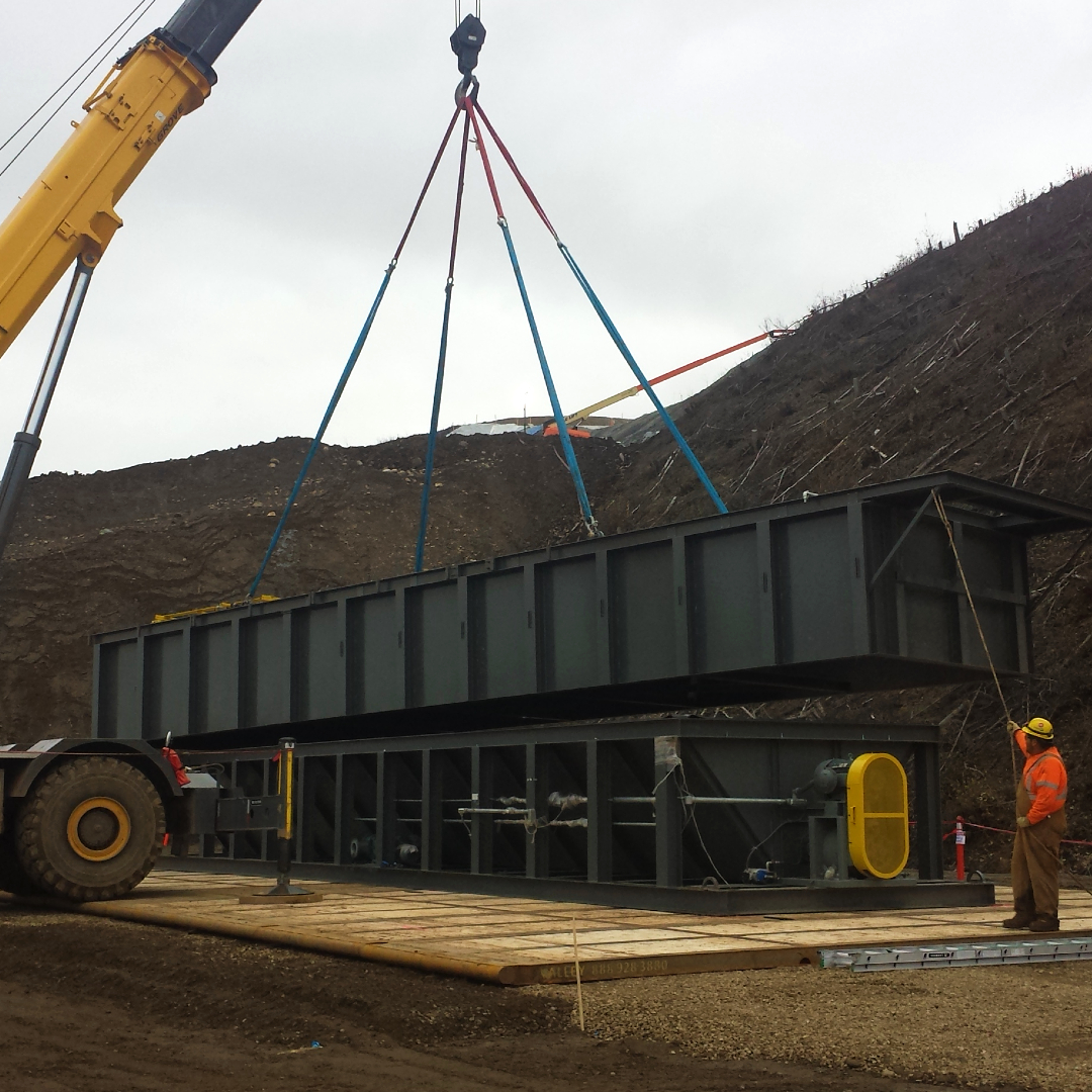 A stationary rectangular industrial water clarifier being setup with a crane and worker guidance at a job site.