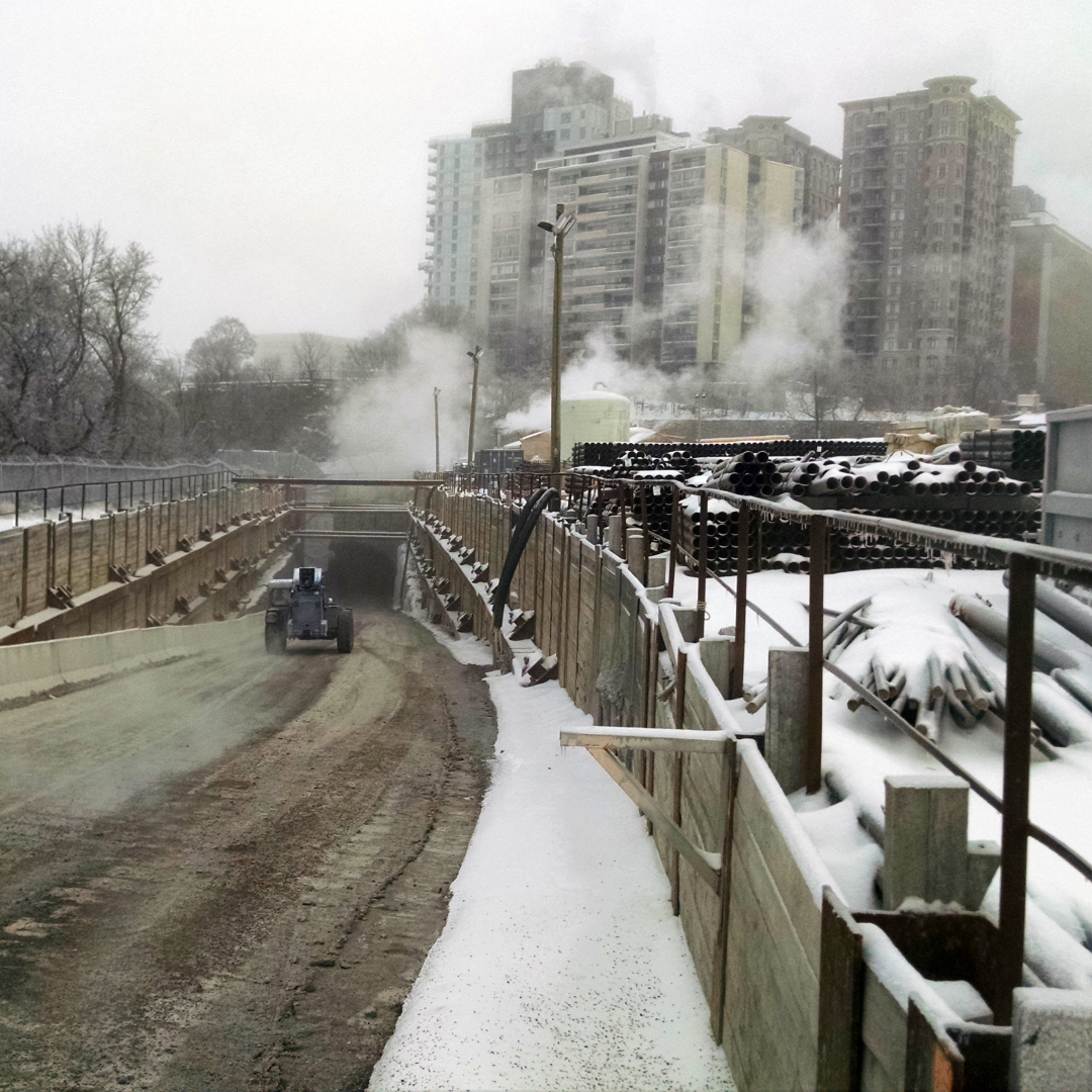 A machine driving down into a tunnel below buildings in the winter.