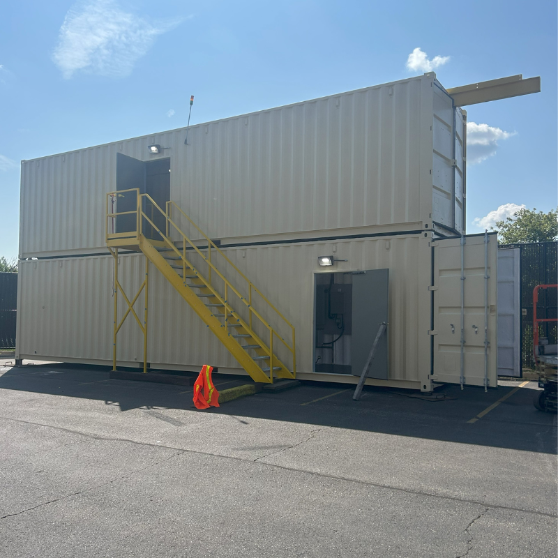 Two beige 40 foot high cube conex boxes stacked on top of each other to house a big bag dry polymer make-down system.