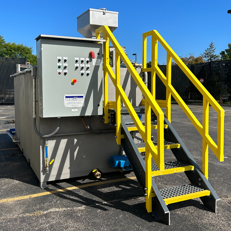 Clearwater Industries standard M-Series dry polymer make-down system with a stainless steel tank, control panel, and access stairs that have safety yellow paint on the hand rails.