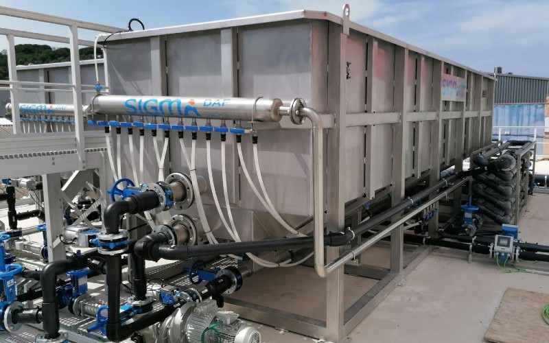 A 304 stainless steel DAF clarifier tank with black piping and other equipment connected to it.