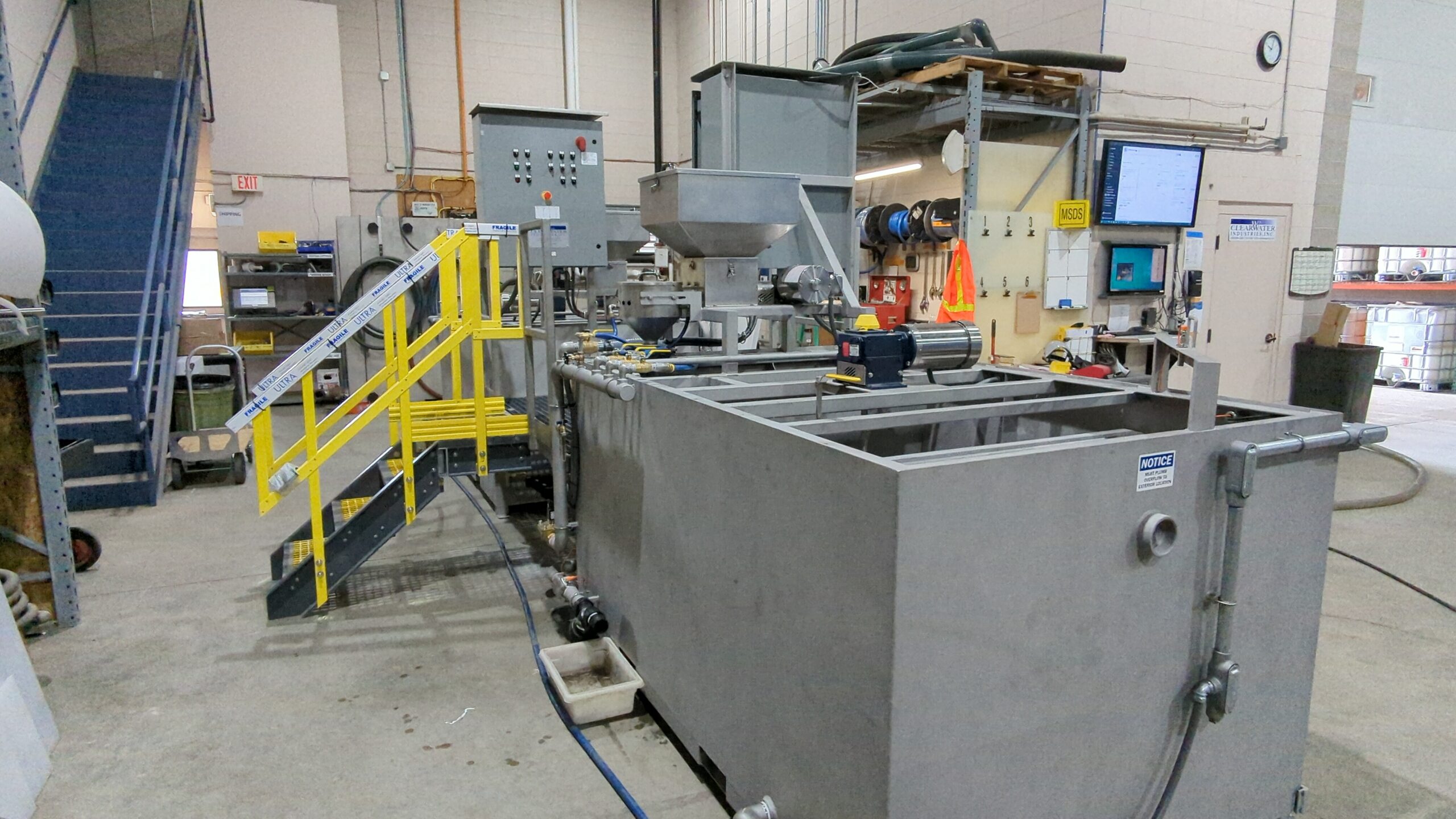 A closer view of rectangular stainless steel tanks with a yellow painted staircase leading up to control panels.